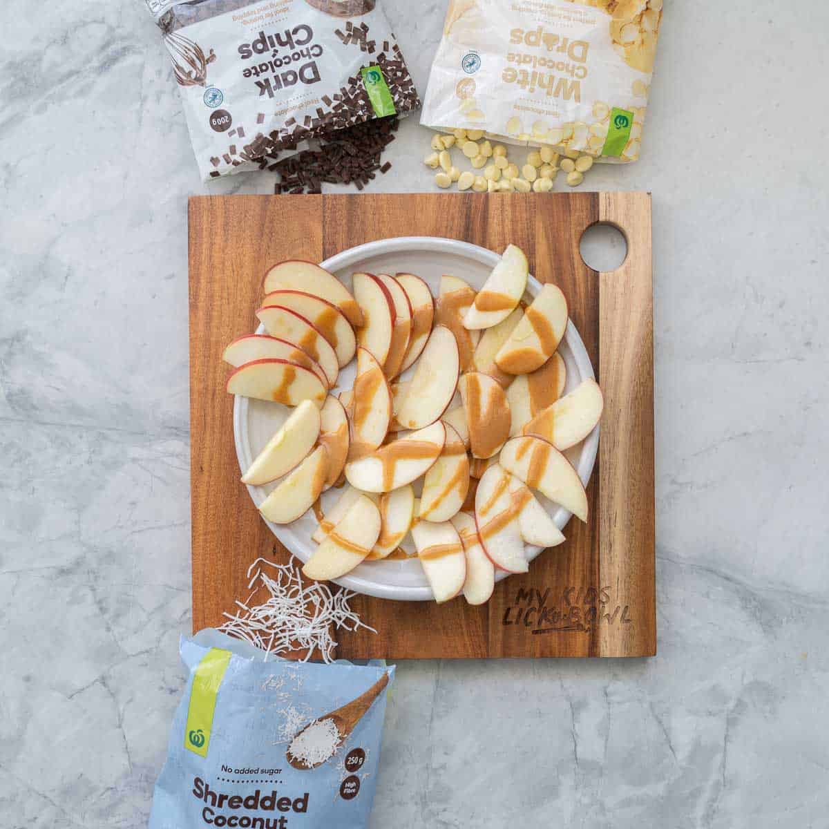 Apple slices arranged on a round white platter drizzled with caramel