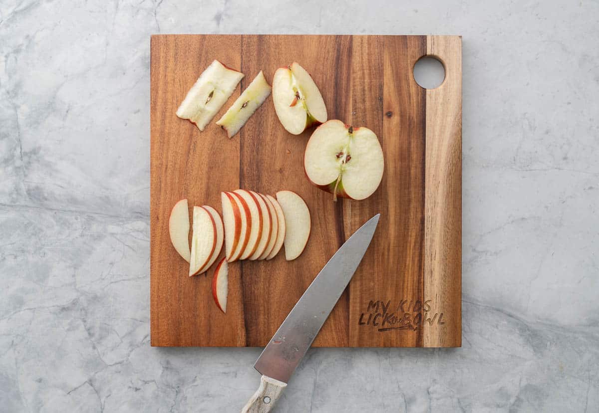 Apple slices, apple quarters, halves and cores on a wooden chopping board with a sharp knife.