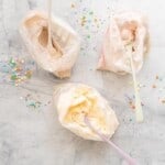 Three ziplock bags of ice cream with spoons on a marble bench scattered with sprinkles.