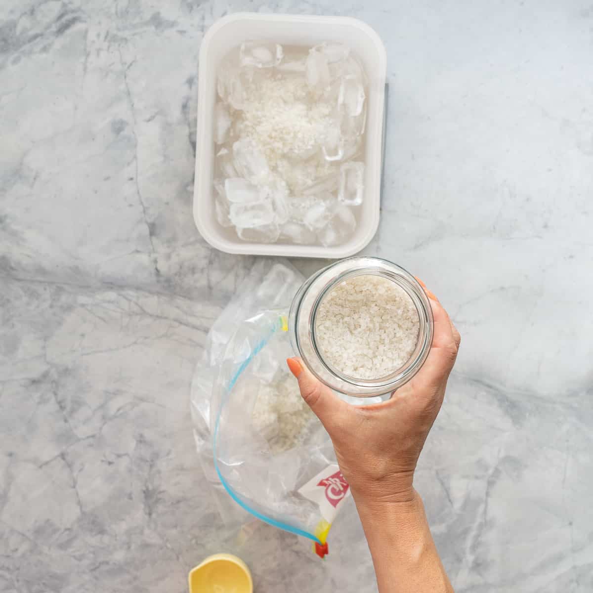 A jar of rock salt being poured into a large zip loc bag of ice.