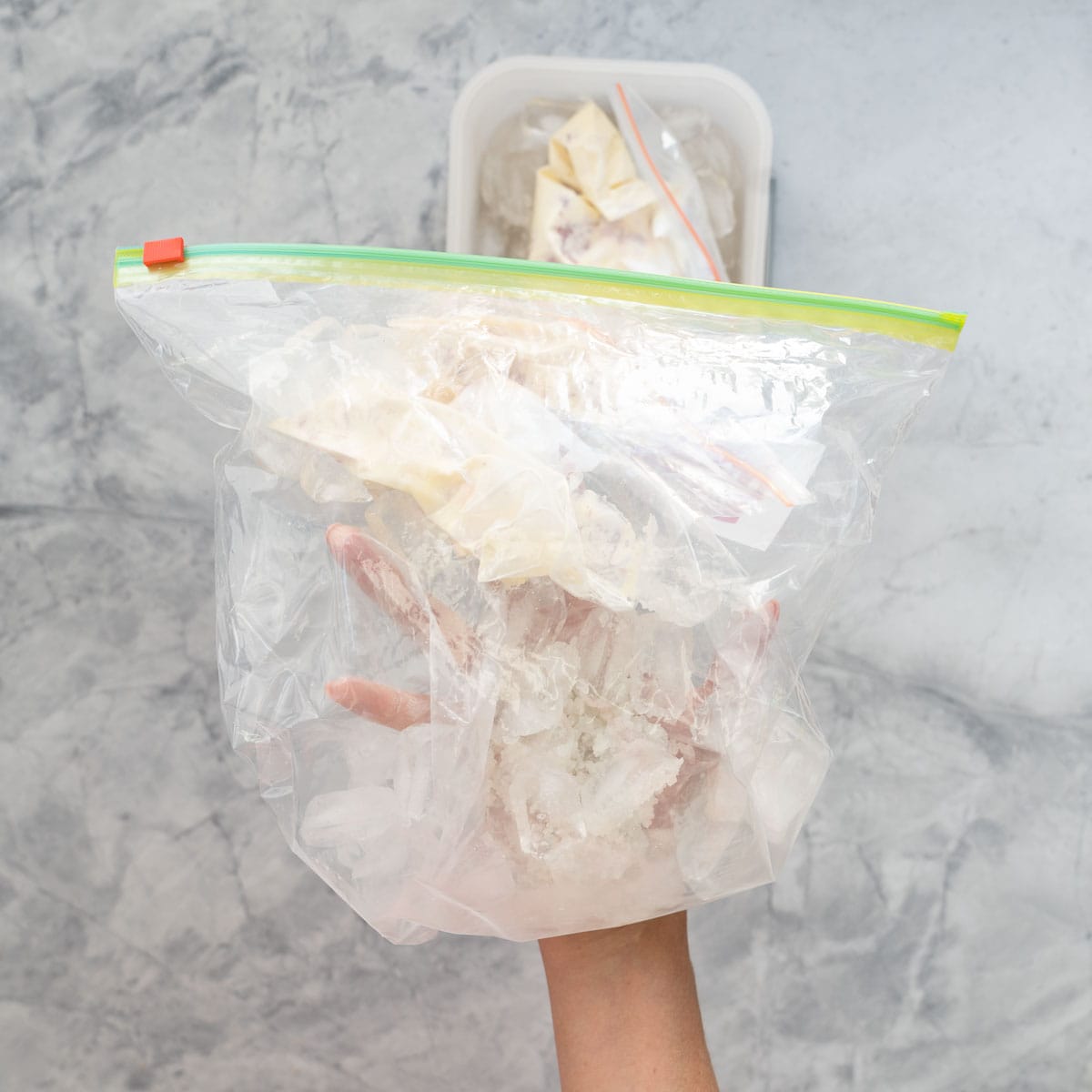 A small zip lock bag of ice cream ingredients inside a big zip lock bag of ice and salt being shaken.