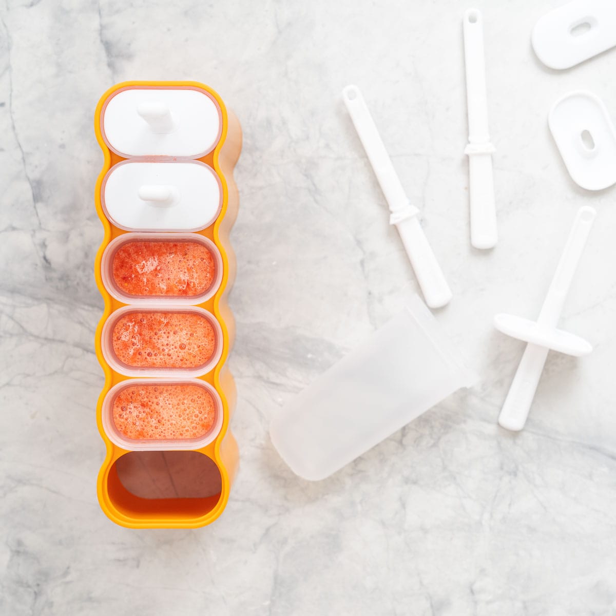 Strawberry popsicle mix poured into popsicle moulds, ready to go into the freezer