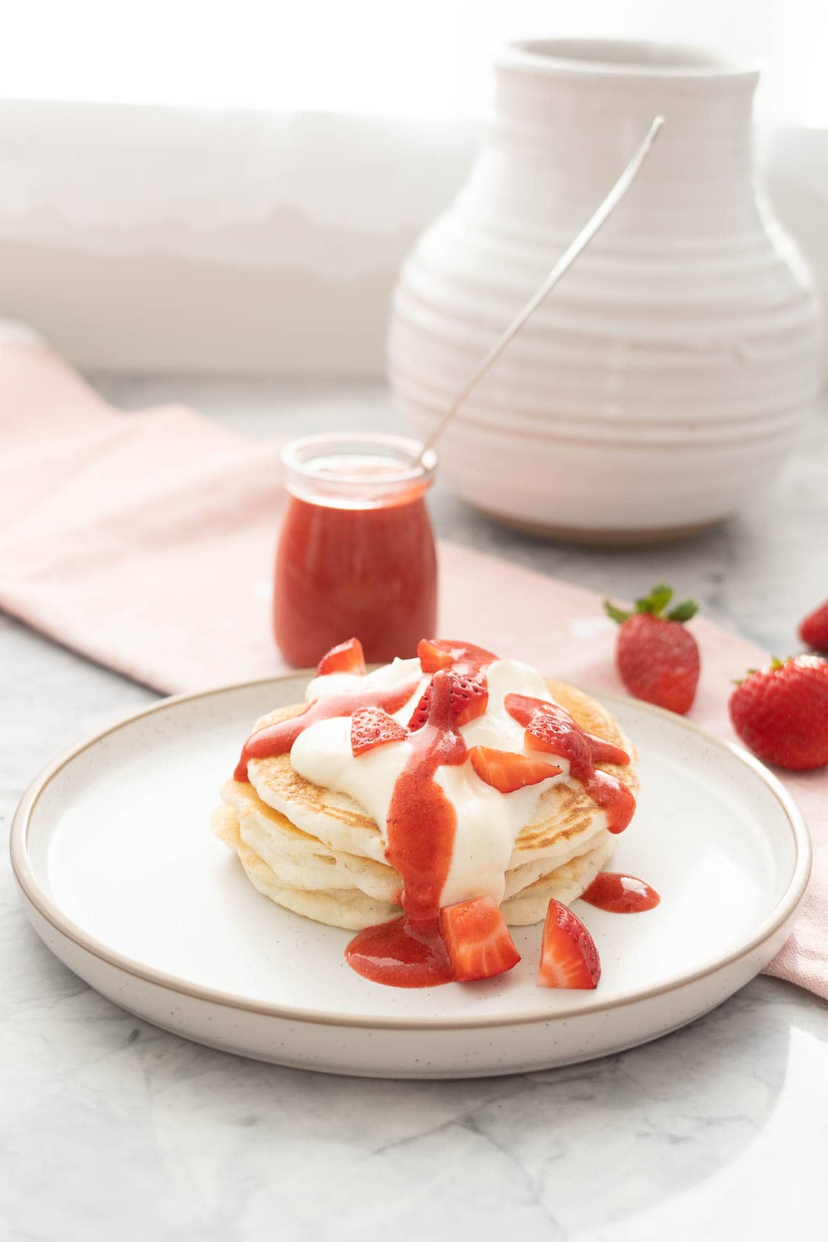 A stack of there pancakes garnished with yoghurt dice strawberries and strawberry puree