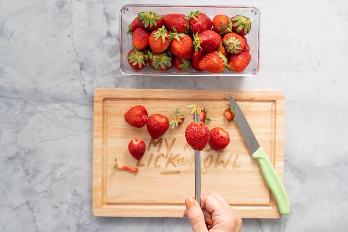 A stainless steel straw being pushed through the bottom of a strawberry to hull it.
