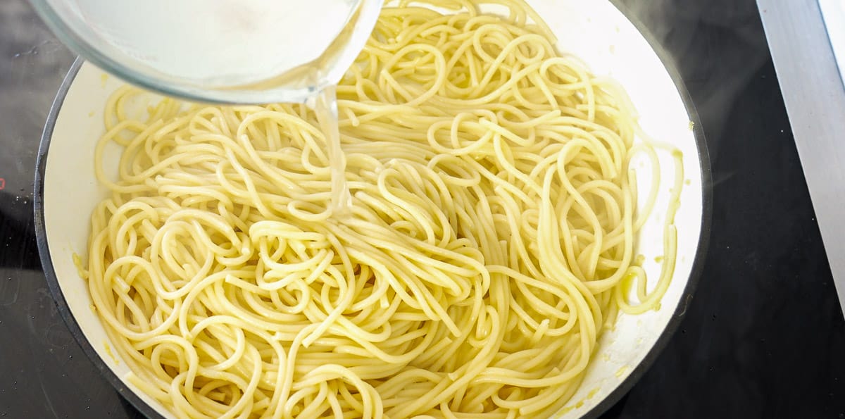 cooked and drained pasta added to the butter and garlic pan with reserved pasta water being poured back into it