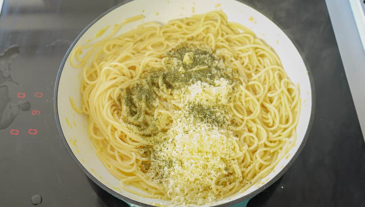 Cheese and seasoning added to the pan full of pasta, garlic and butter