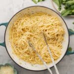 A ceramic dutch oven filled with butter coated spaghetti