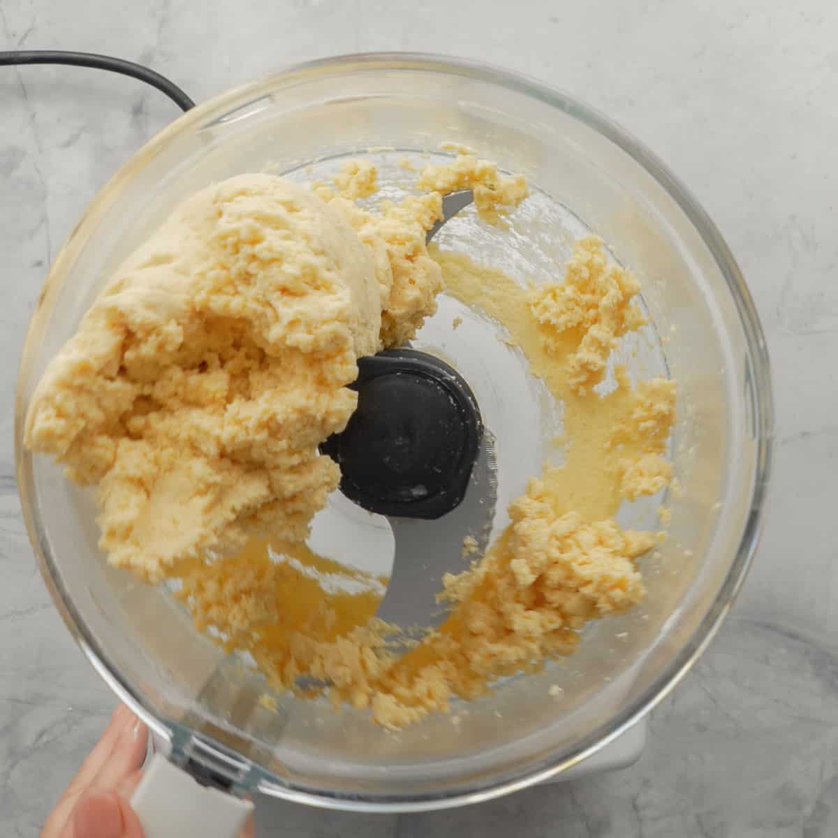 A food processor sitting on the bench with the ingredients mixed together creating the cheese cracker dough