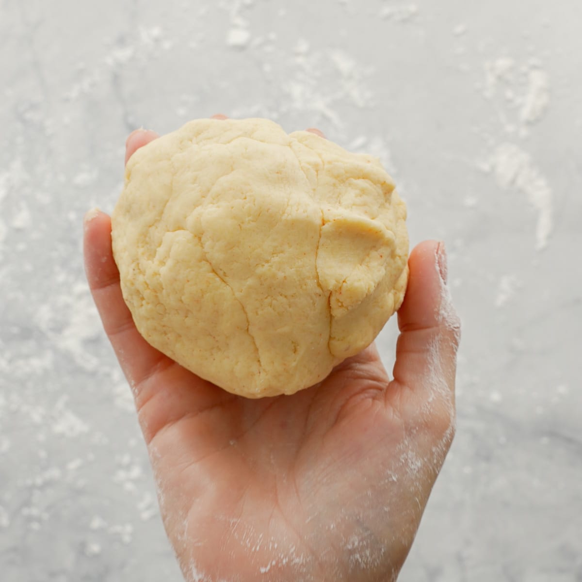 A hand holding the cheese cracker dough above the bench