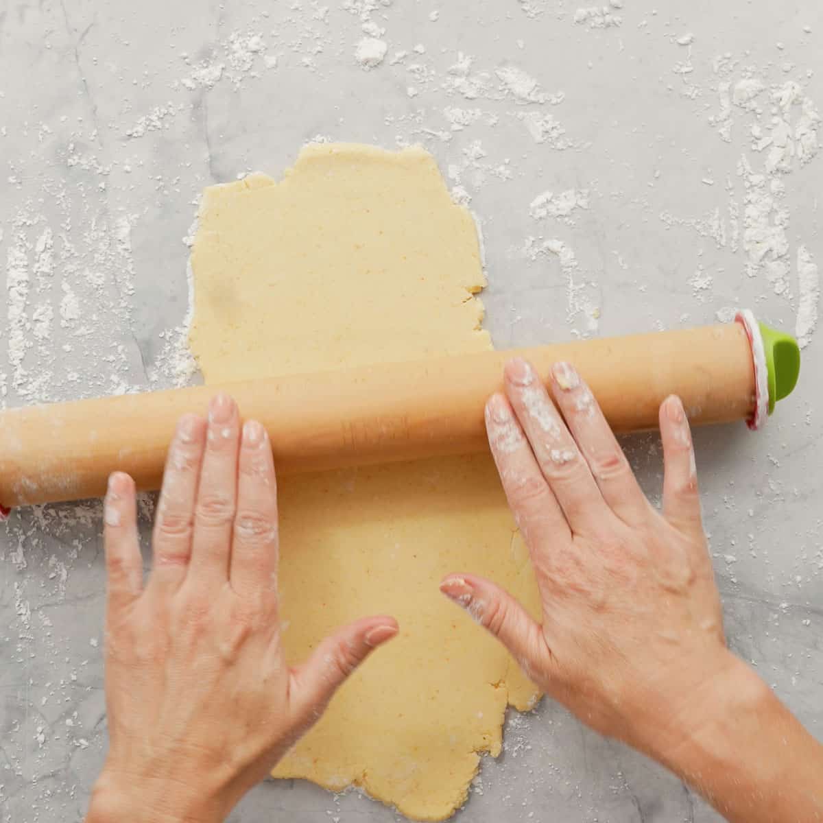 Two hands rolling a rolling out the cheese cracker dough with a rolling pin
