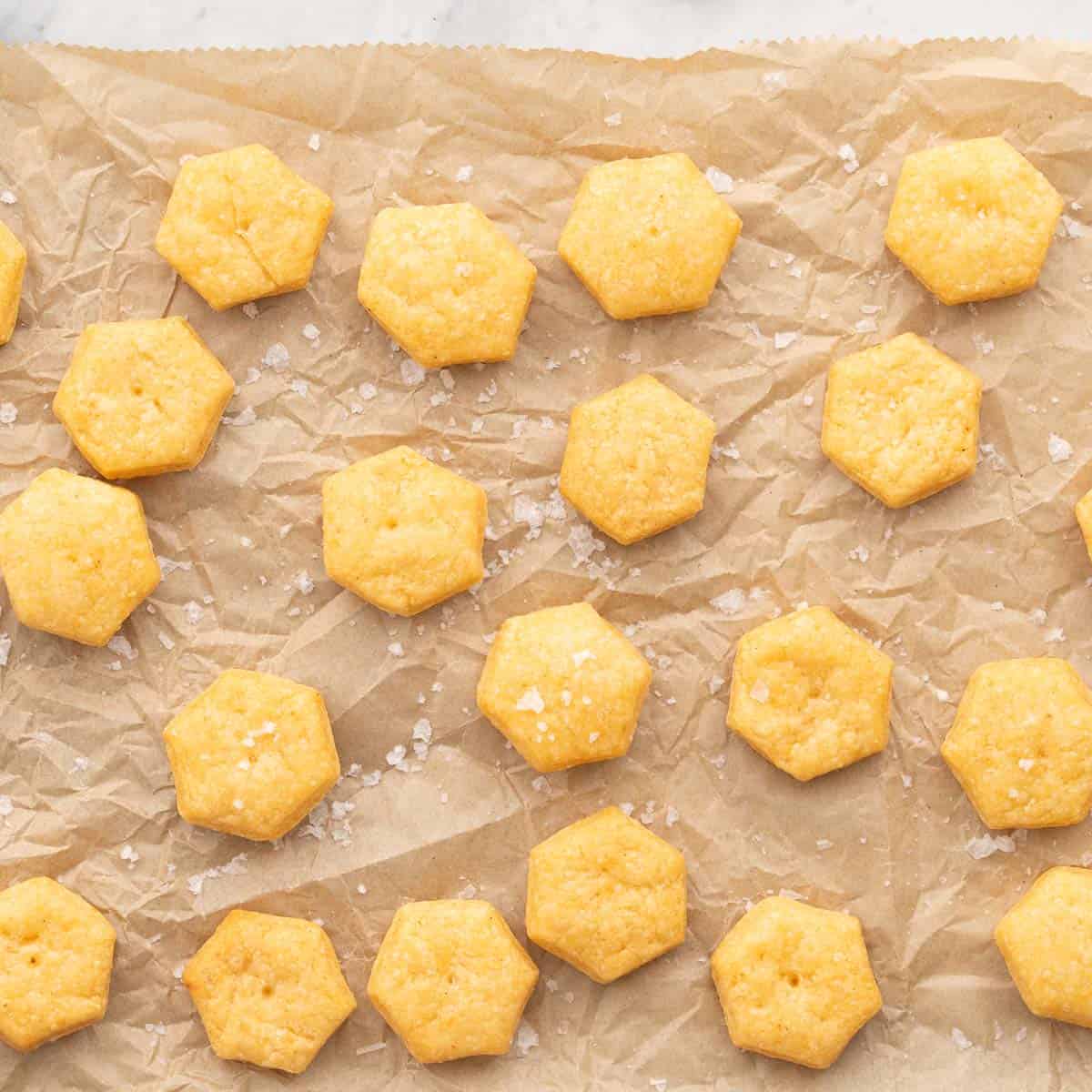 Golden brown baked cheese crackers resting on a lined baking tray with a sprinkling of sea salt on the top.