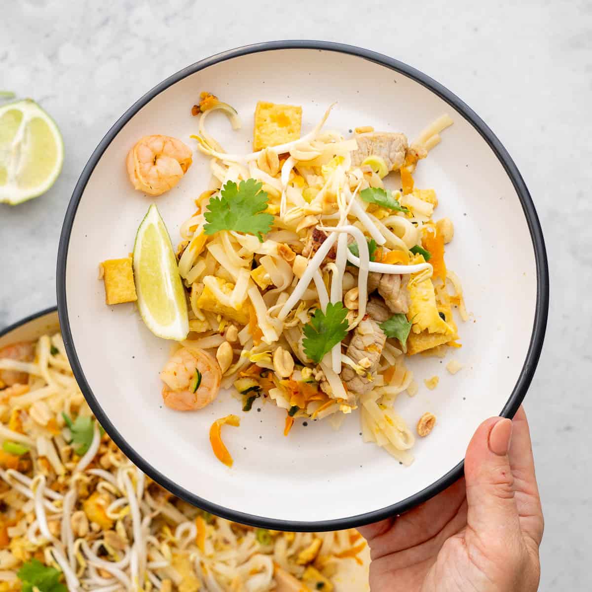 A white plate with black rim holding pad this, with bean sprouts, lime wedges and prawns visible