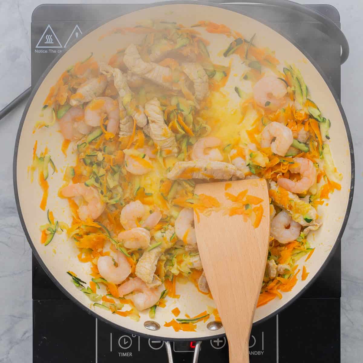 Stir fried pork, prawns and grated vegetables in a ceramic wok.