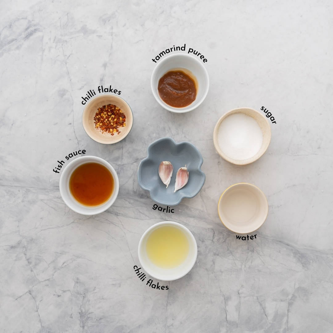 Seven ingredients to make pad thai sauce in small bowls with text overlay labels.