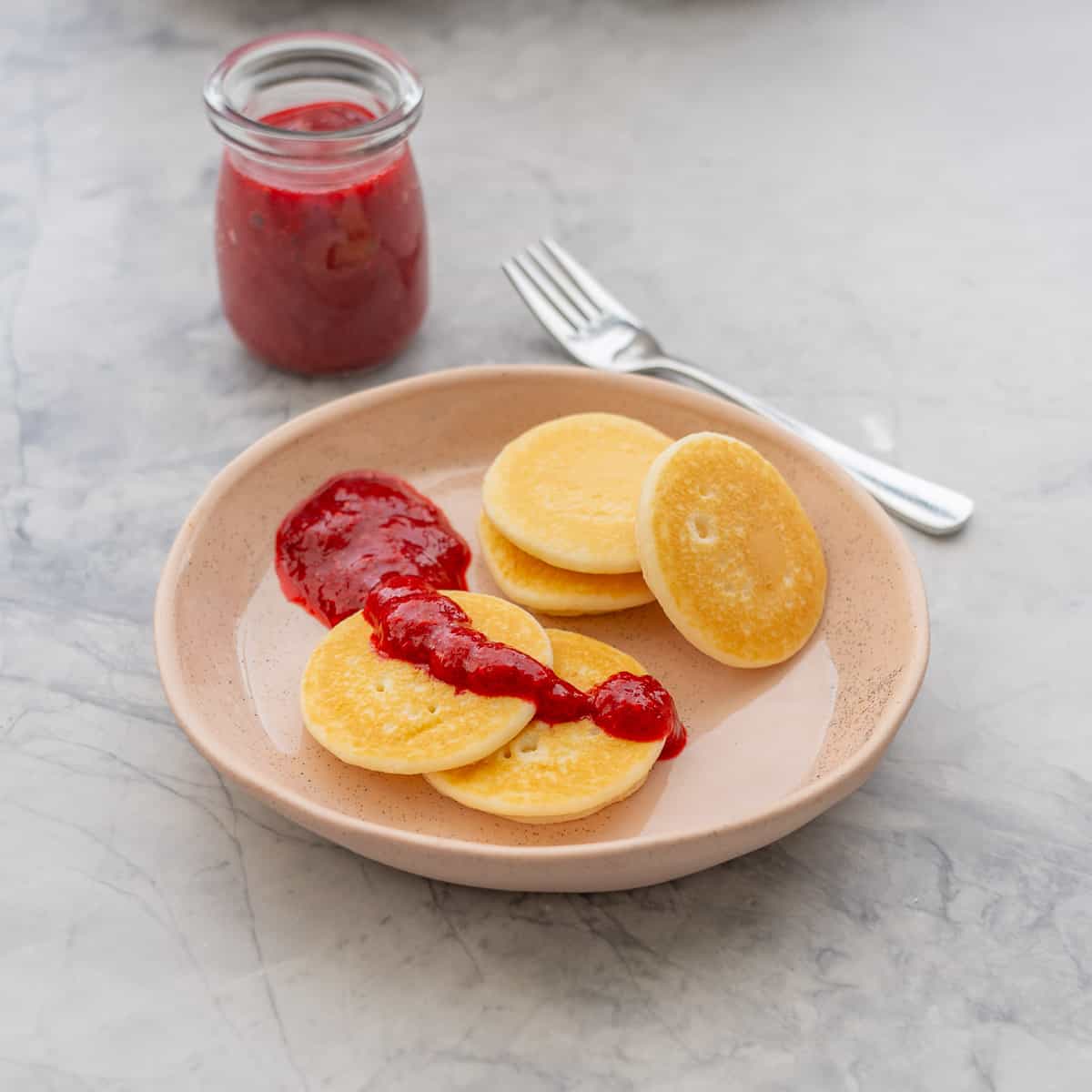 Raspberry puree drizzled over golden pickets served on a small ceramic plate which is sitting next to a small jar of the raspberry puree