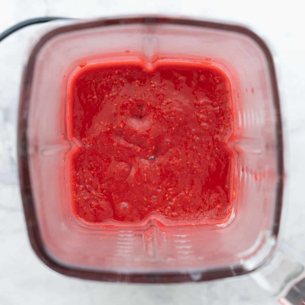 Smooth raspberry puree in a blender resting on the bench
