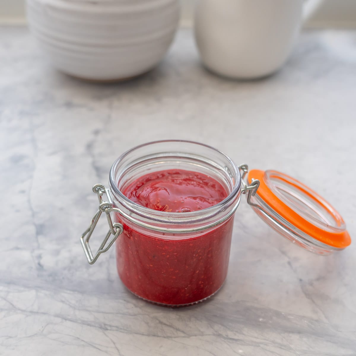 A small jar filled with raspberry puree resting on the bench