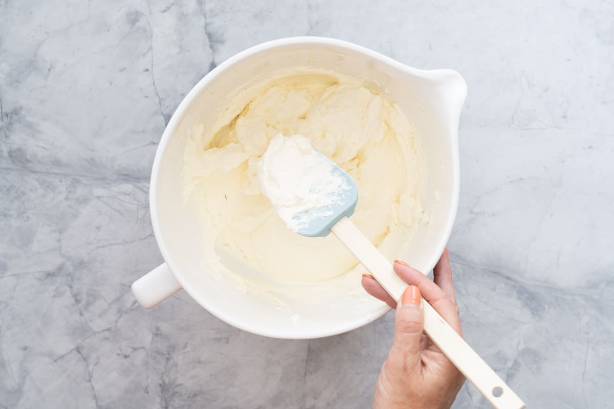 A large ceramic mixing jug of whipped cream with a blue silicone spatula.