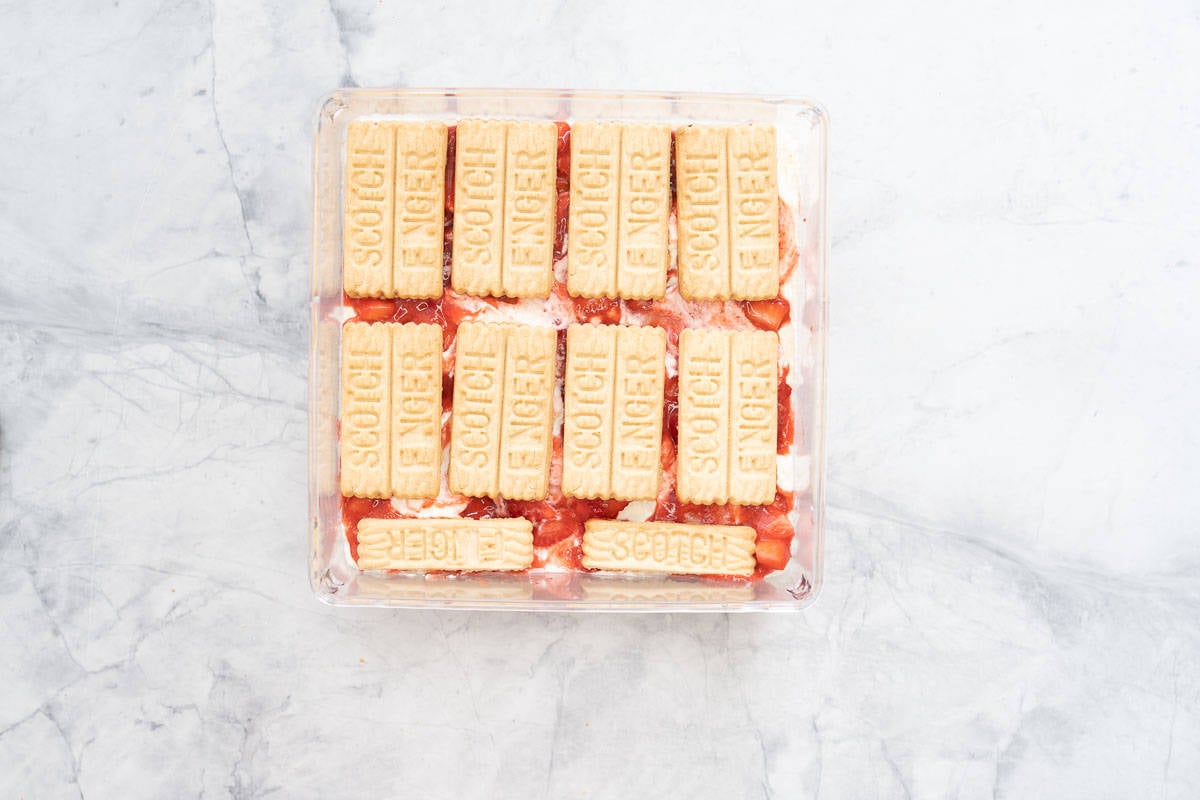 Scotch fingers arranged in a layer on top of strawberries, strawberry puree and whipped cream.