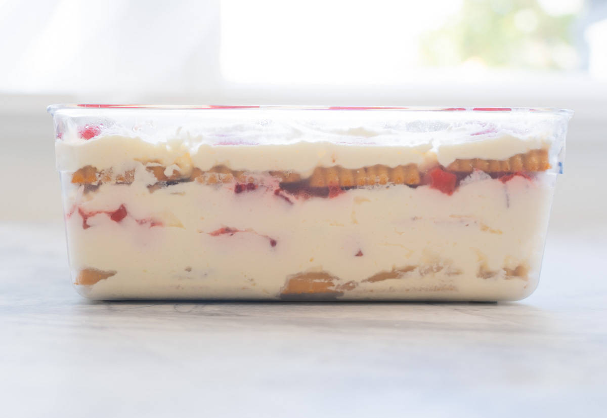 A strawberry shortcake ice box cake in a glass container, the layers of cream cookies and strawberries visible.