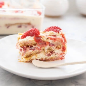 A piece of a strawberry shortcake ice box cake on a plate with a white bamboo spoon.