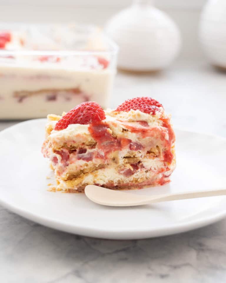A piece of a strawberry shortcake ice box cake on a plate with a white bamboo spoon.