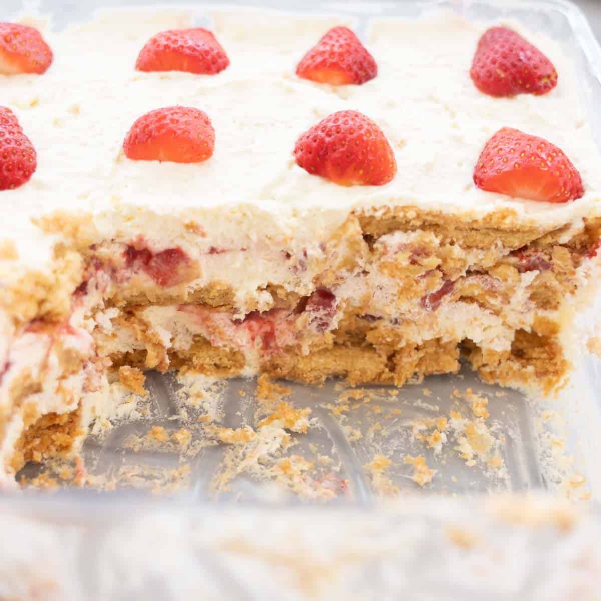 Looking into a container of a strawberry shortcake, some pieces removed so you can see the layers of biscuit, fruit and cream.