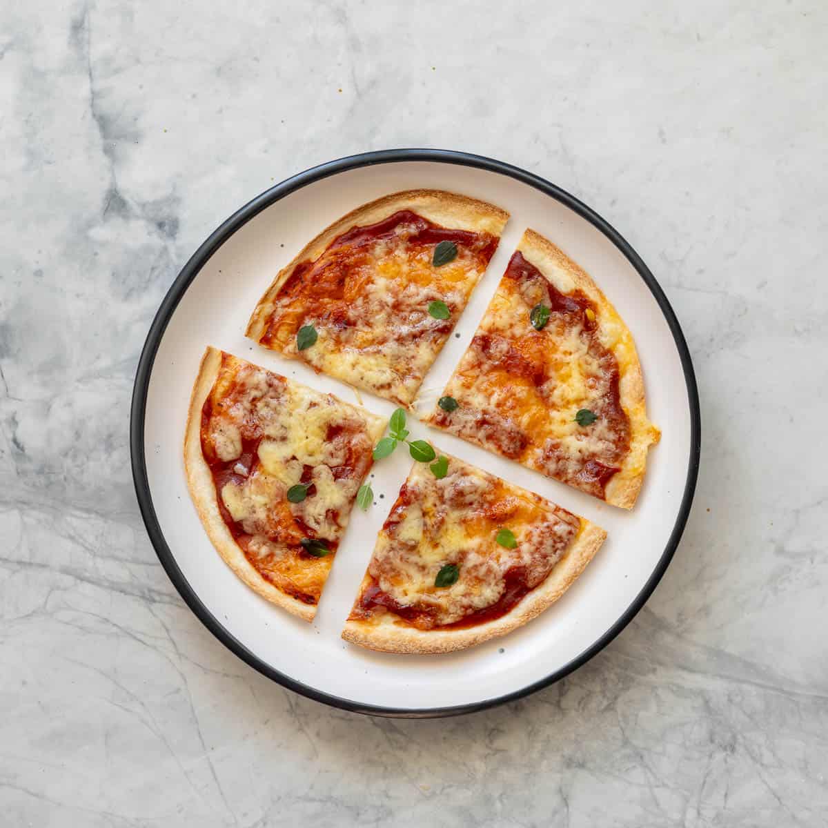 A tortilla pizza cut into quarters and served on a plate which is resting on the bench