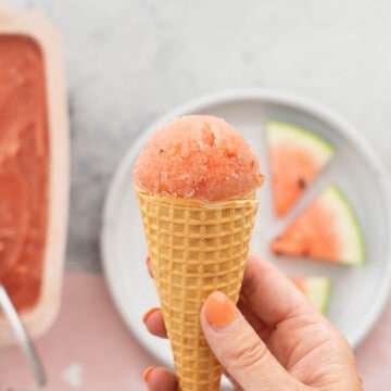 A waffle cone topped with pink sorbet being held up to the camera.