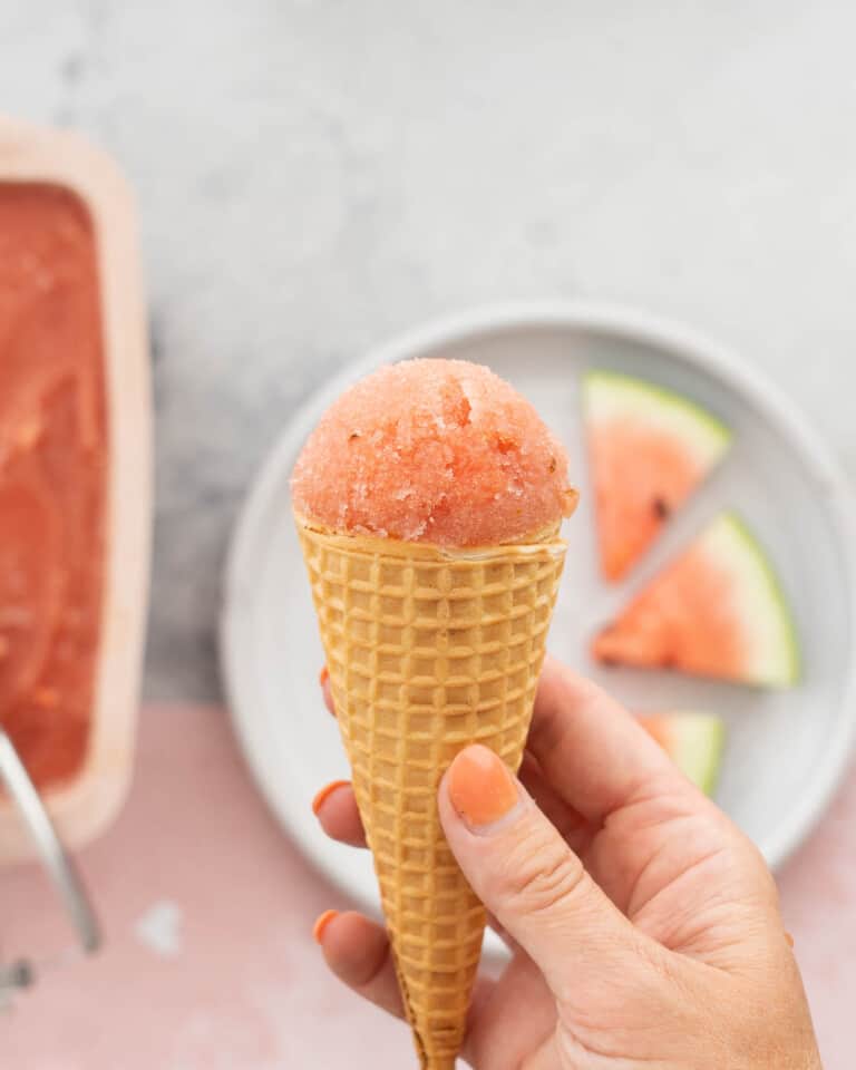 A waffle cone topped with pink sorbet being held up to the camera.