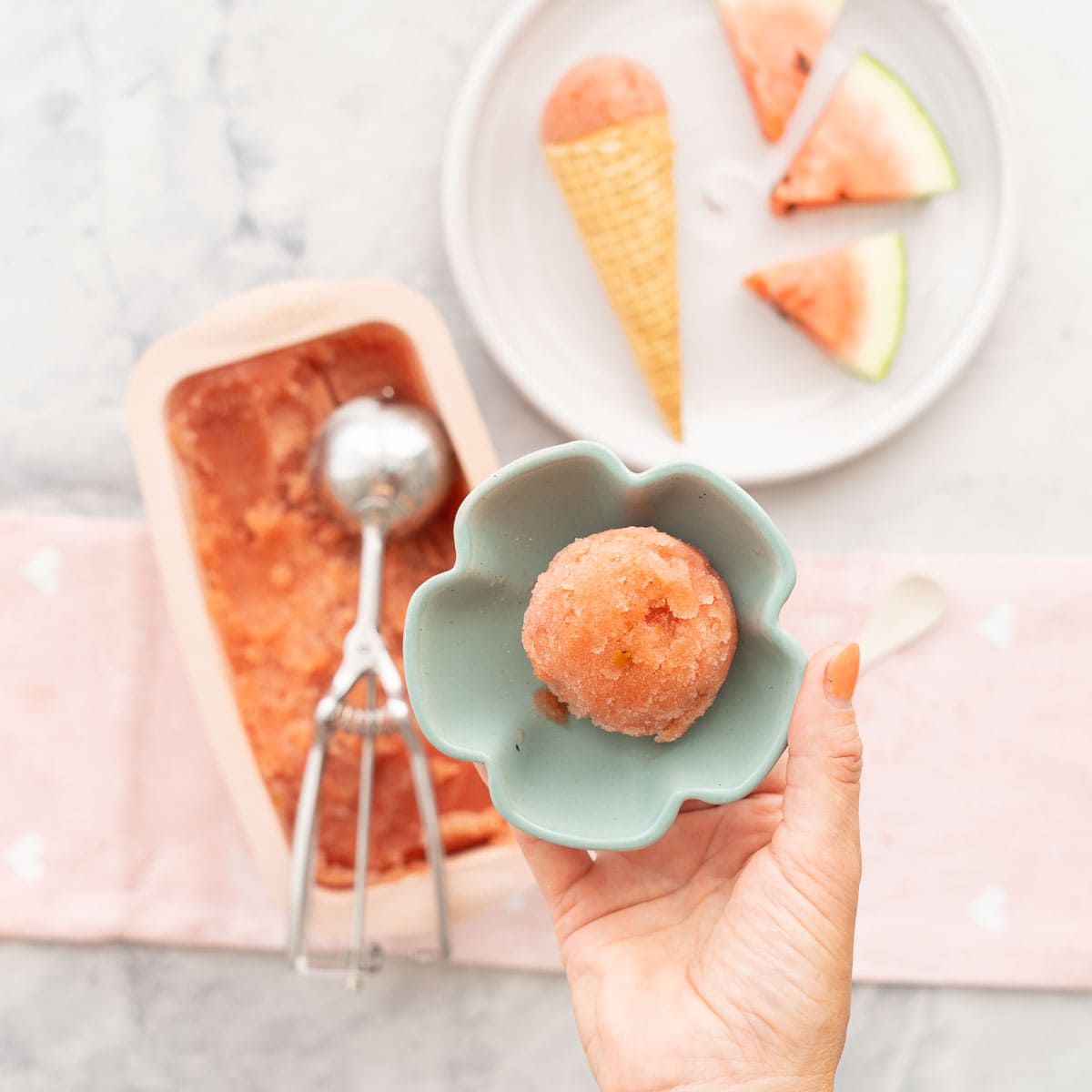 A small blue ceramic flower shaped bowl with a scoop of sorbet inside it being held up to the camera