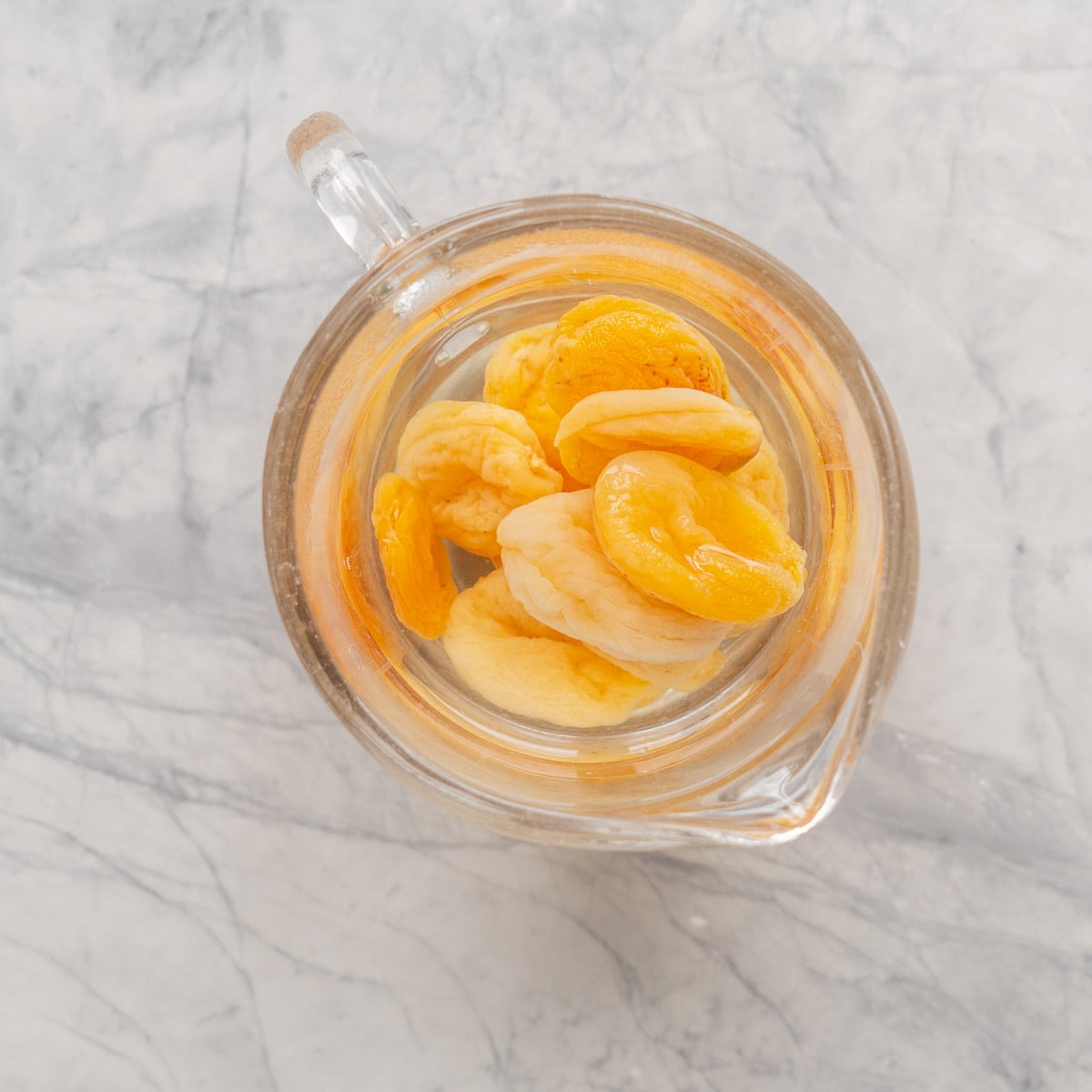 A glass jug of apricots soaking in water.