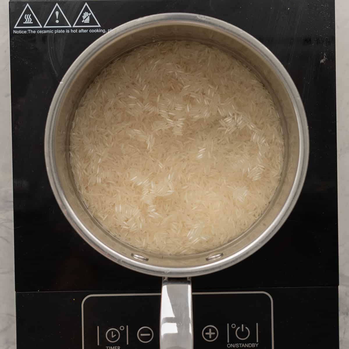 Basmati rice and water in a saucepan on the cooktop with the lid on.