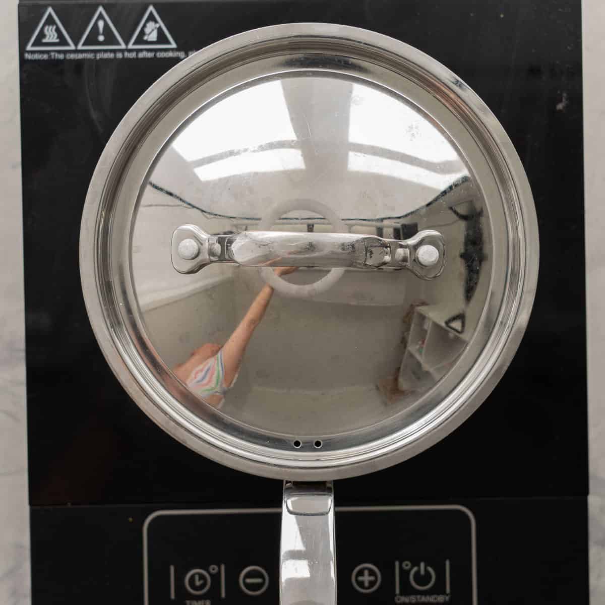 A pot with a lid on it sitting on the cooktop with the lid on.