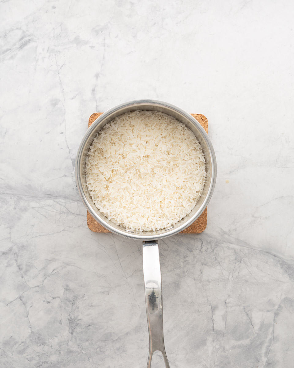 Steamed basmati rice in a saucepan resting on a cork matt sitting on the bench.