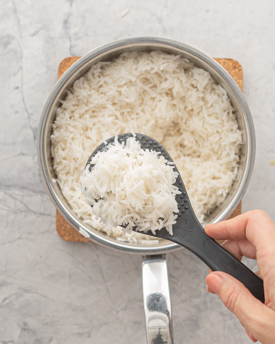 Steamed basmati rice in a saucepan resting on a cork matt sitting on the bench.