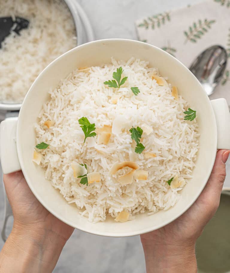 A large bowl of Basmati rice, sprinkled with parsley and a scattering of toasted almonds, held above the bench by a pair of hands