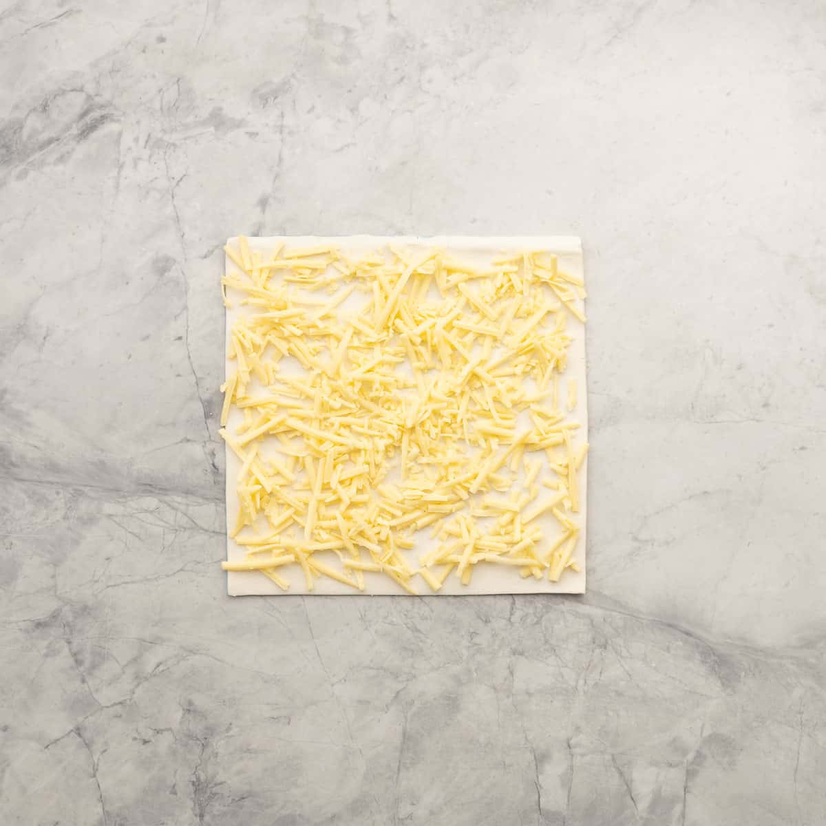 A square sheet of puff pastry covered with a layer of grated cheese.