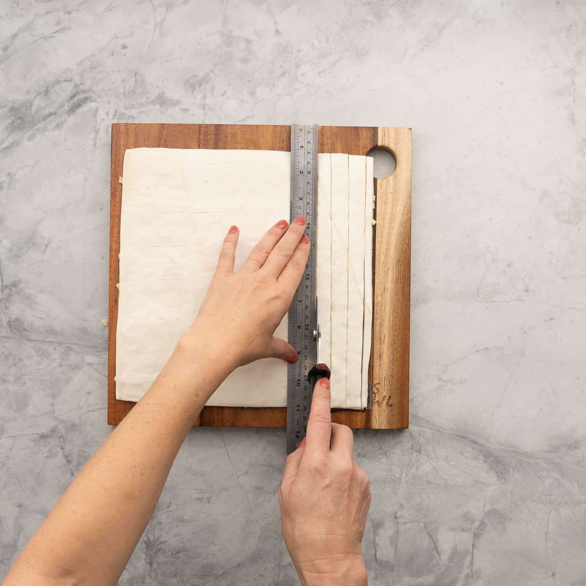 Puff pastry being measured with a ruler and cut into even strips with a sharp knife.