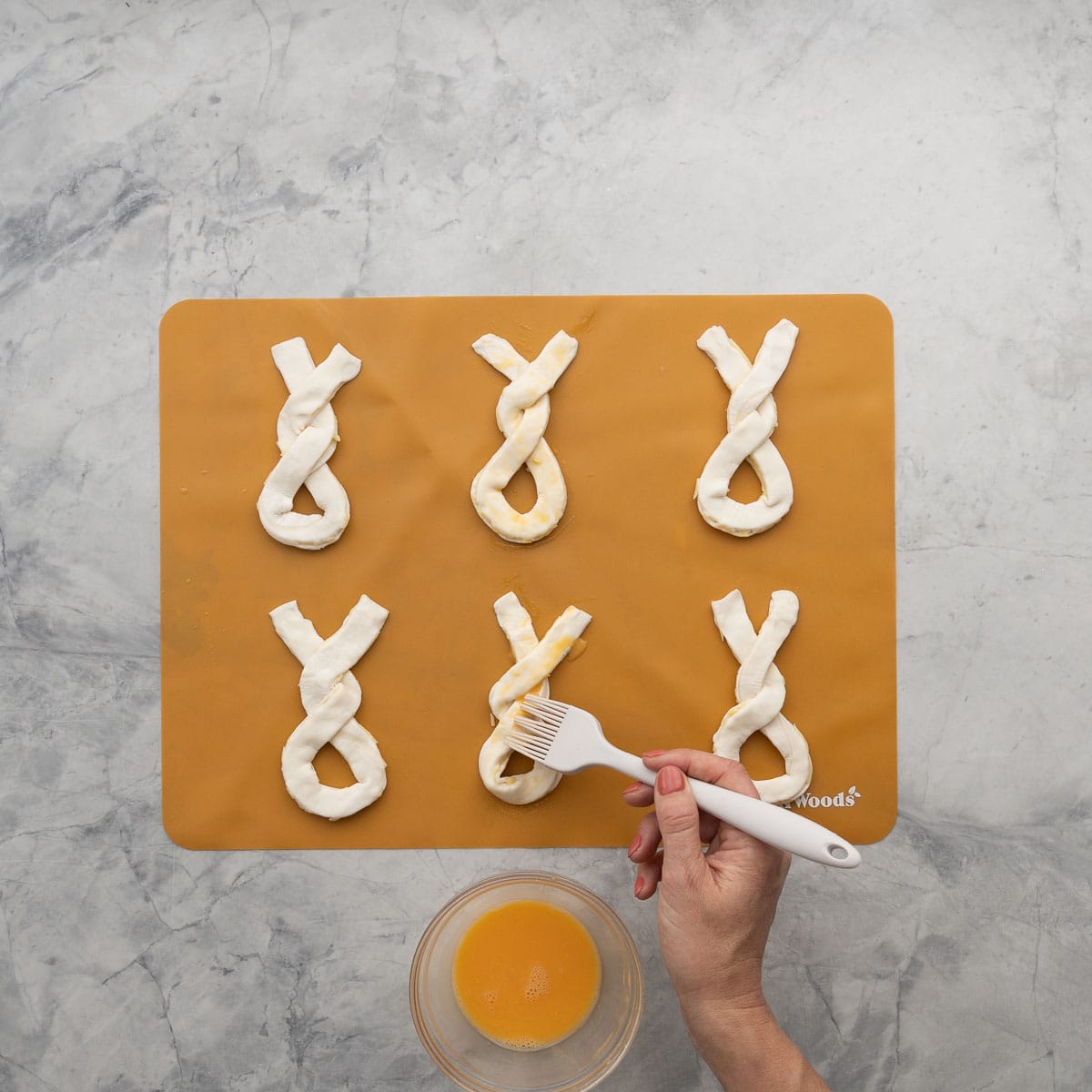 Uncooked puff pastry shapes being brushed with an egg wash.