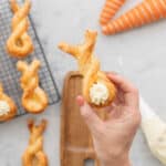 A puff pastry bunny twist with piped cram cheese tail being held up to the camera.