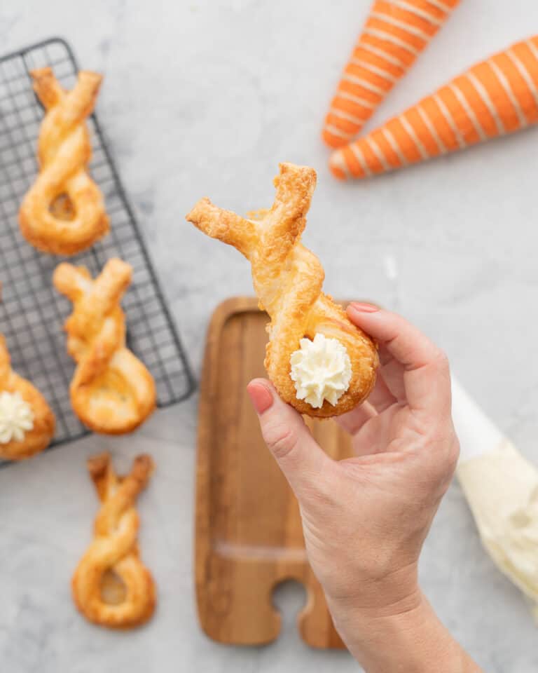 A puff pastry bunny twist with piped cram cheese tail being held up to the camera.