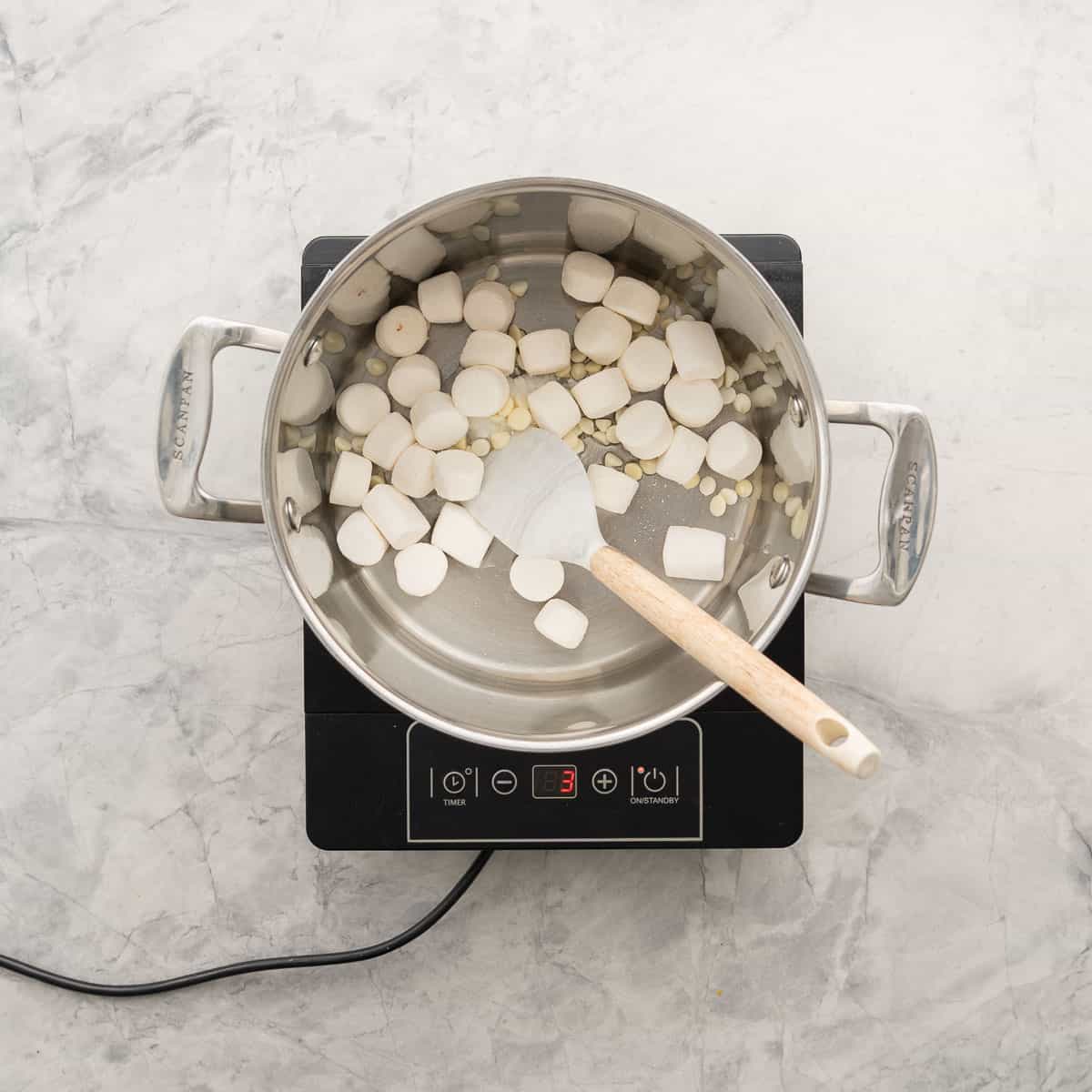 A large sauce pan of marshmallows, white chocolate chips and coconut oil on a portable element.