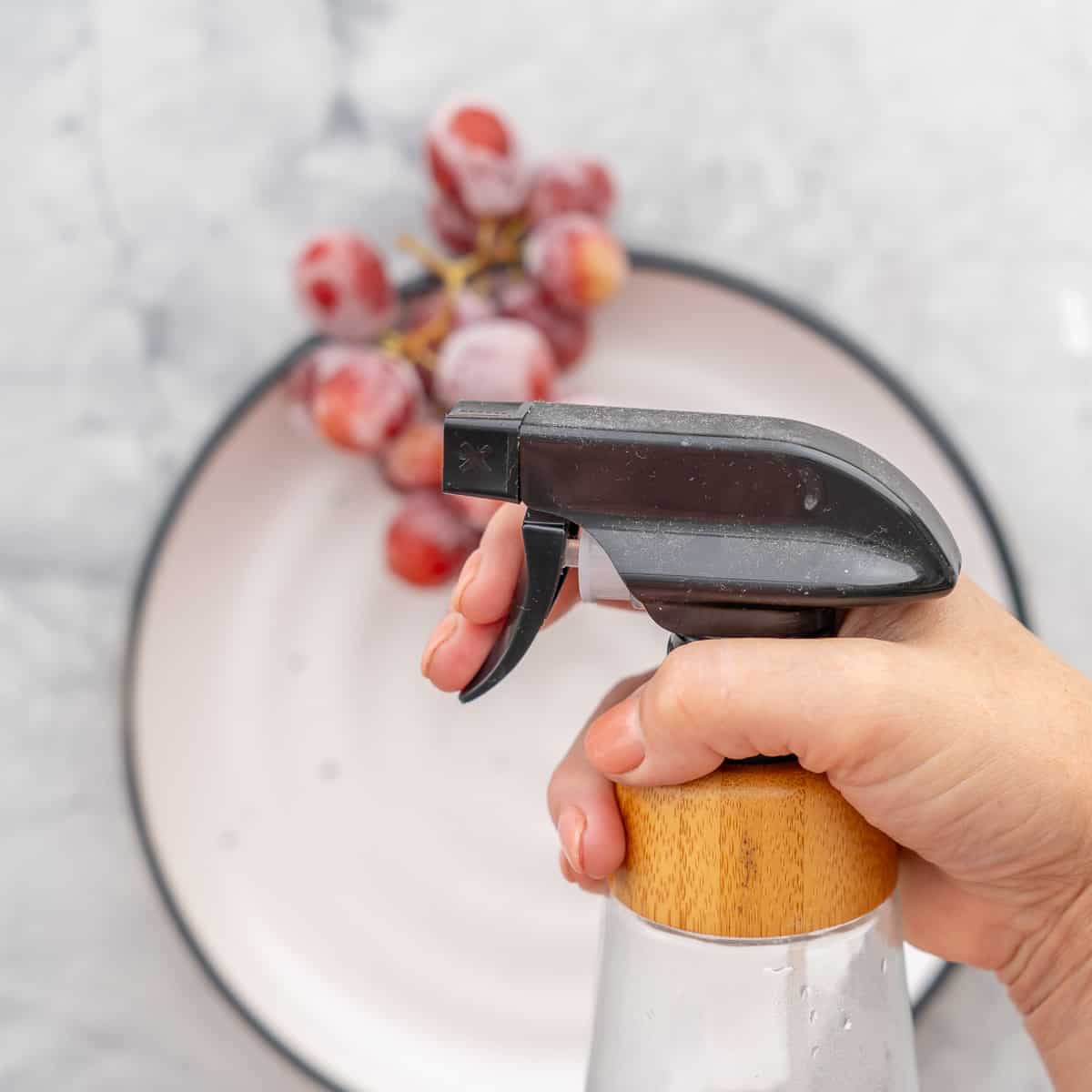 A spray bottle filled with water held above the bunches of grapes below.