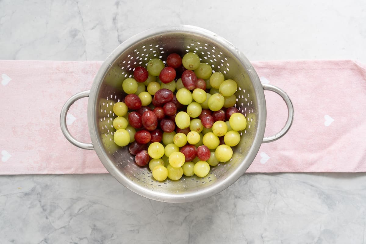 Fresh green and red grapes washed in a colander resting on a tea towel on the bench