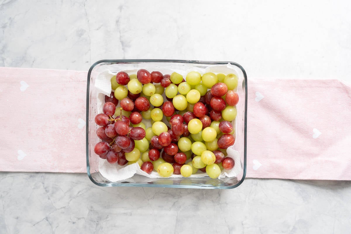 Fresh green and red grapes sitting on a lined glass storage container.