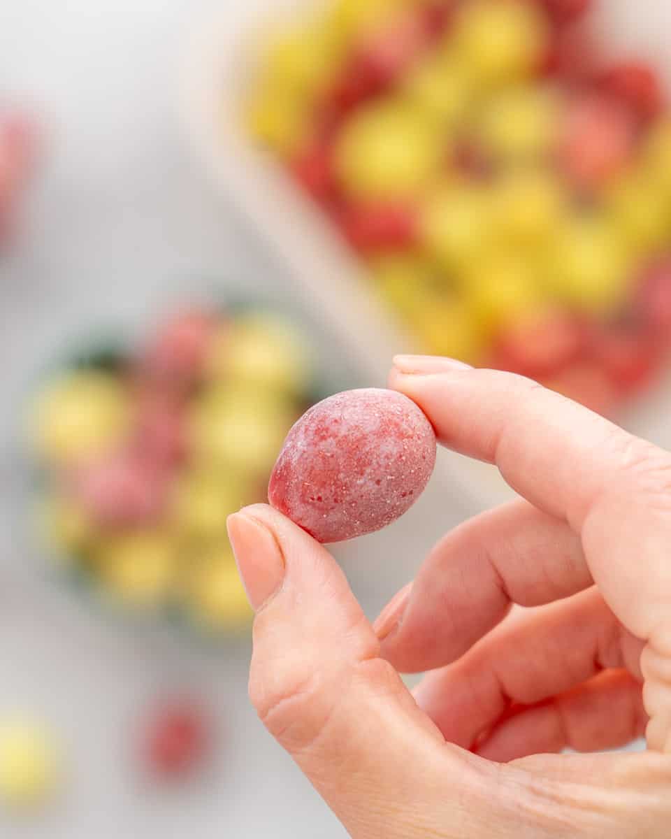 A hand holding up one frozen red grape above the rest of the container below.