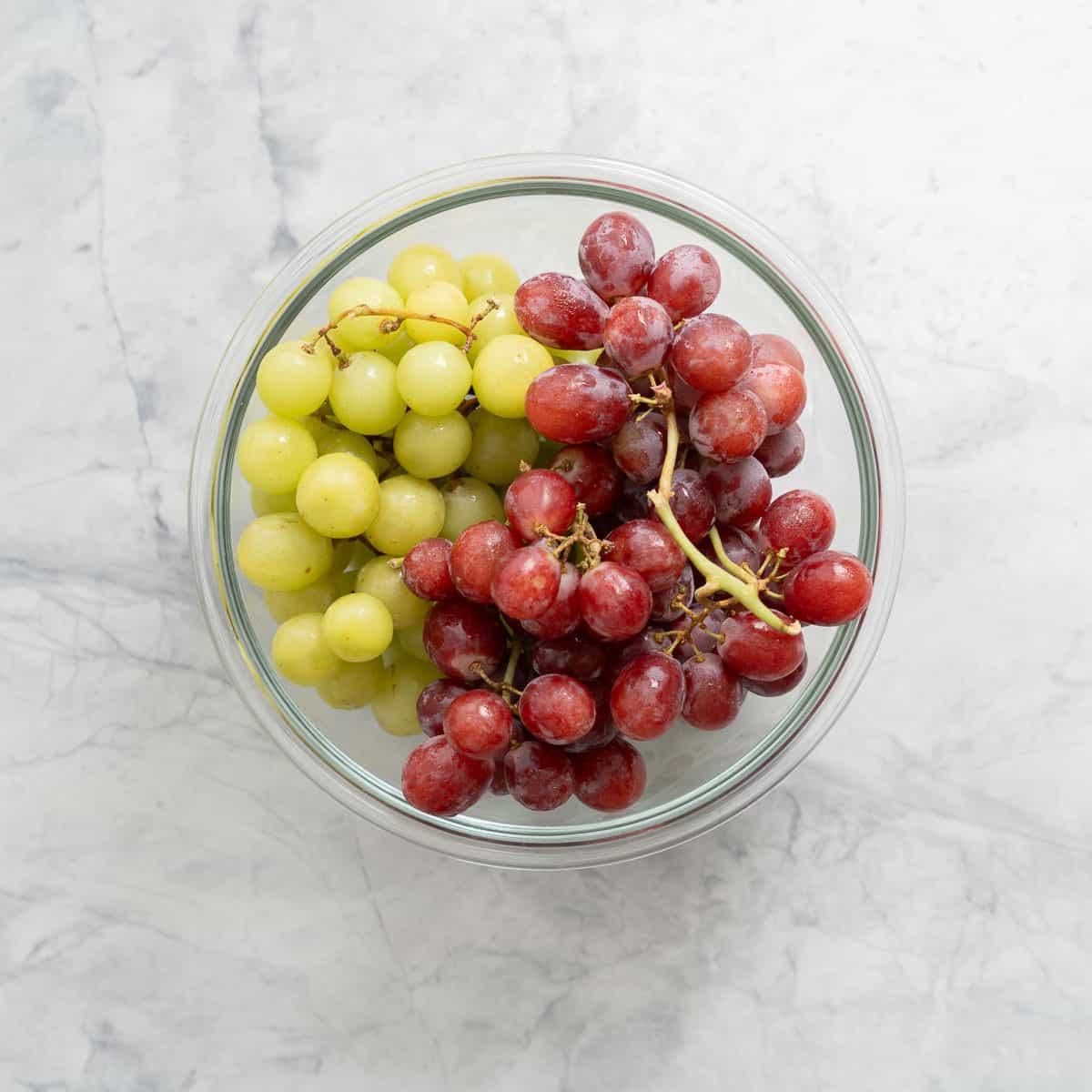 Fresh bunches of green and red grapes in a large glass bowl sitting on the bench