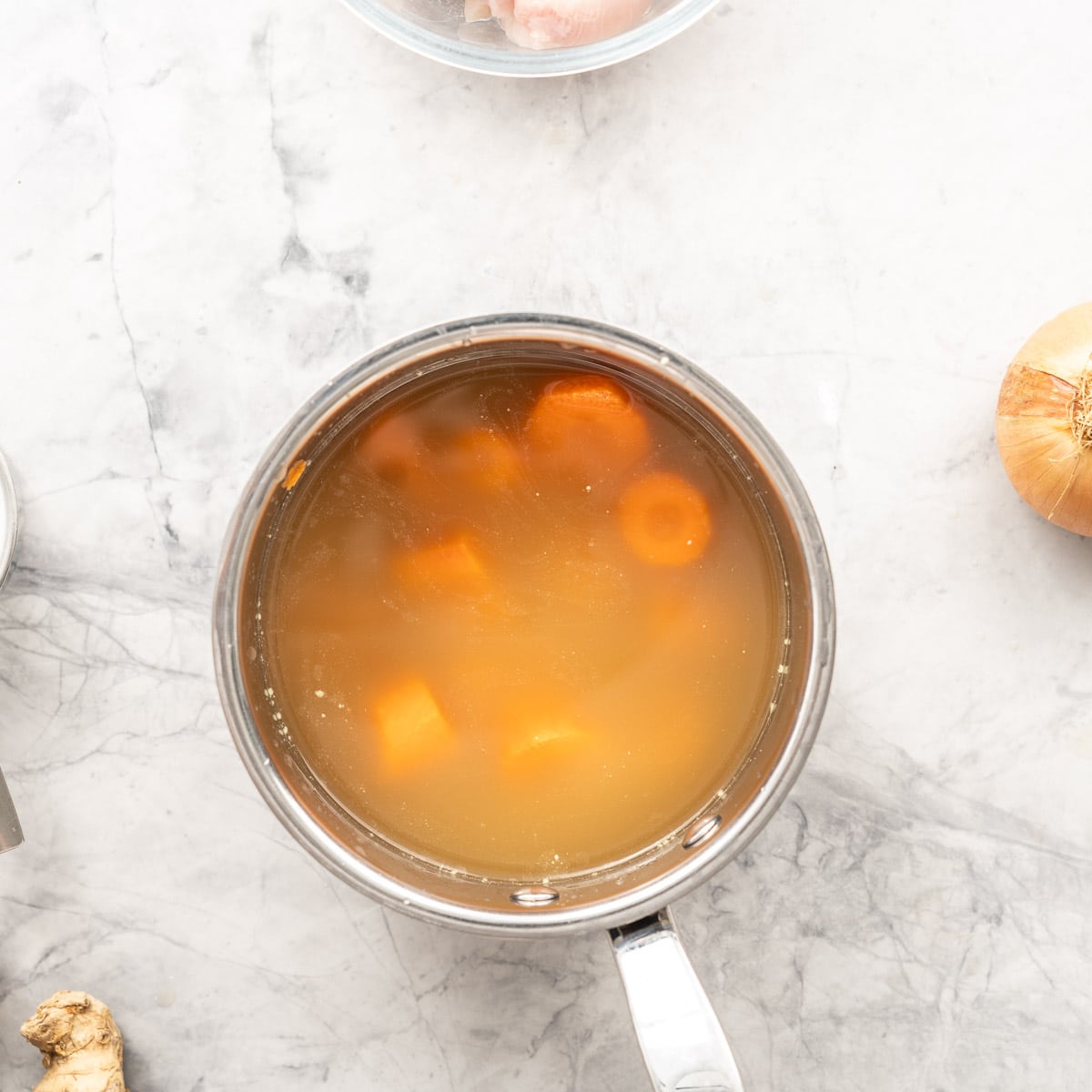 Red lentils, carrots and stock in a pot resting on the bench 