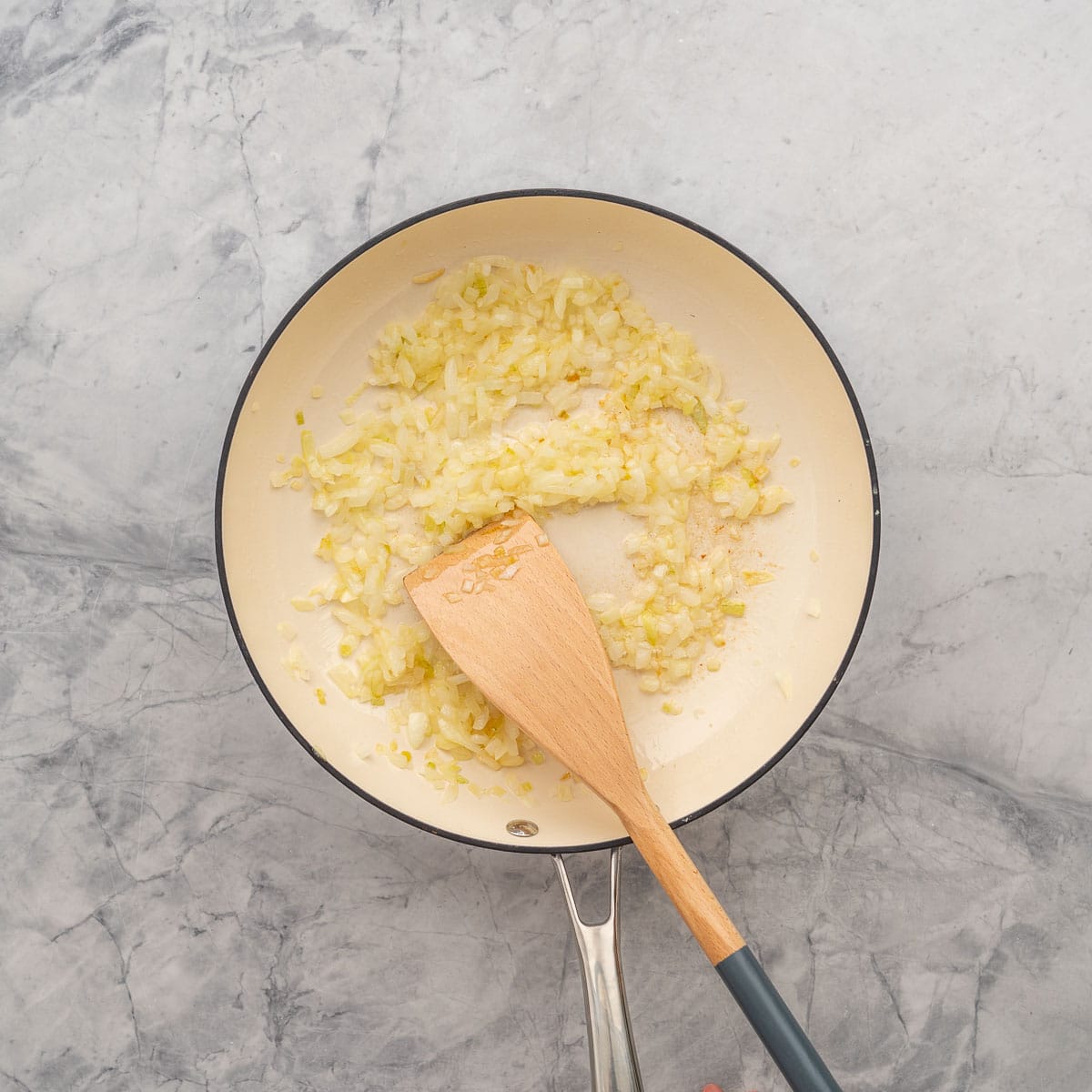 Onions sauteed in a pan with oil, resting on the bench with a wooden spoon resting on the side. 